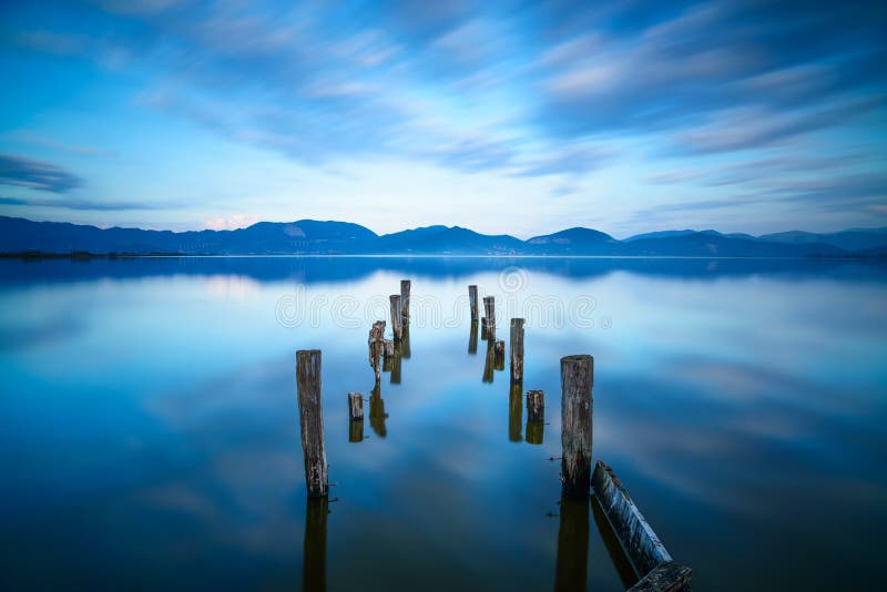 El embarcadero o el embarcadero de madera permanece en una reflexión azul de la puesta del sol y del cielo del lago en el agua. Ve fotografía de archivo libre de regalías El embarcadero o el embarcadero de madera permanece en una reflexión azul de la puesta del sol y del cielo del lago en el agua. Ve fotografía de archivo libre de regalías