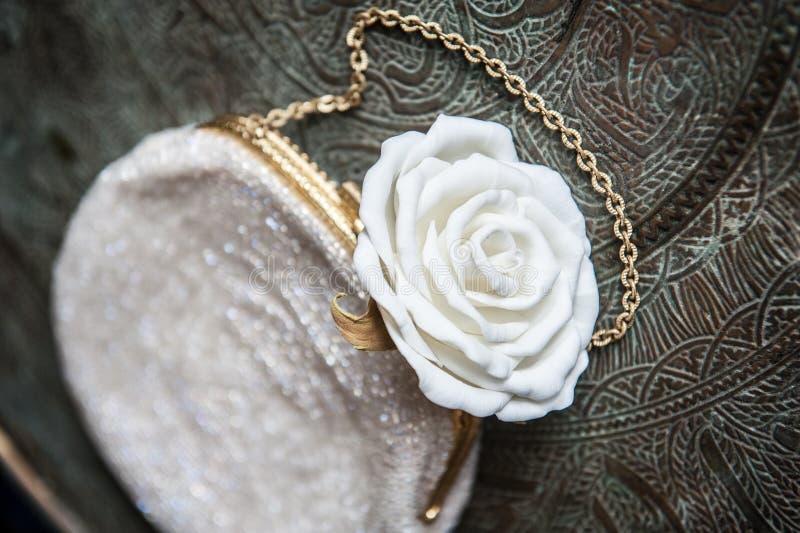 El embrague de las mujeres con la rosa del blanco en la bandeja de cobre amarillo con un ornamento fotos de archivo El embrague de las mujeres con la rosa del blanco en la bandeja de cobre amarillo con un ornamento fotos de archivo