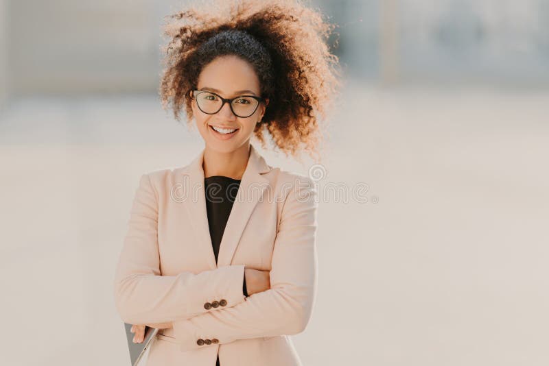 El empresario de sexo femenino alegre confiado con el pelo rizado del Afro, mantiene los brazos doblados, utiliza la tableta mode fotografía de archivo El empresario de sexo femenino alegre confiado con el pelo rizado del Afro, mantiene los brazos doblados, utiliza la tableta mode fotografía de archivo