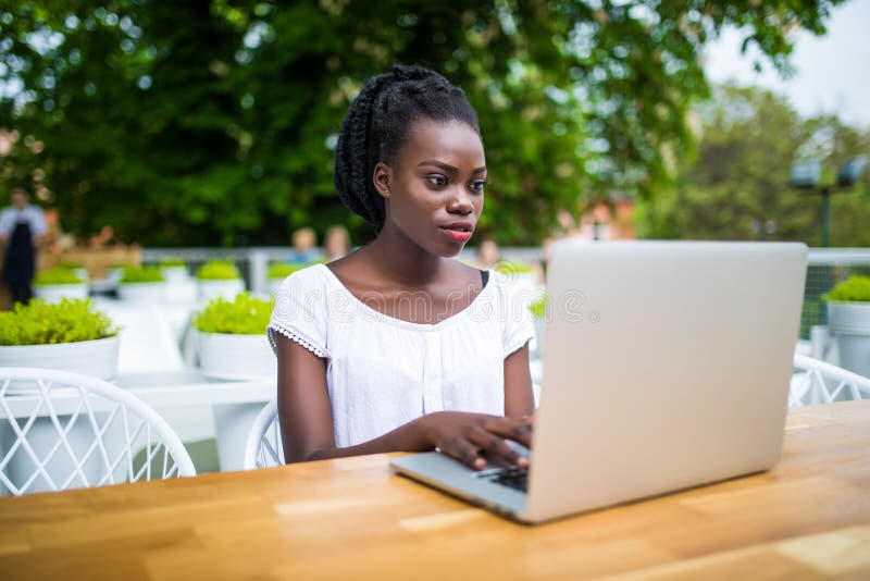 El empresario de sexo femenino negro joven hermoso se está sentando en barra de la calle y está trabajando remotamente en su proy fotografía de archivo El empresario de sexo femenino negro joven hermoso se está sentando en barra de la calle y está trabajando remotamente en su proy fotografía de archivo