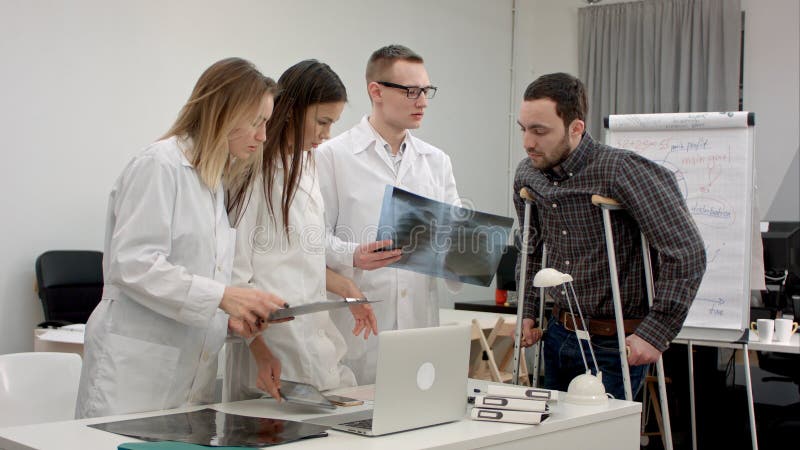El equipo de doctores que explican la radiografía resulta al paciente masculino en las muletas imagen de archivo libre de regalías