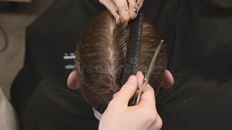 El estilista corta el pelo del hombre utilizando peine y tijeras en la barbería