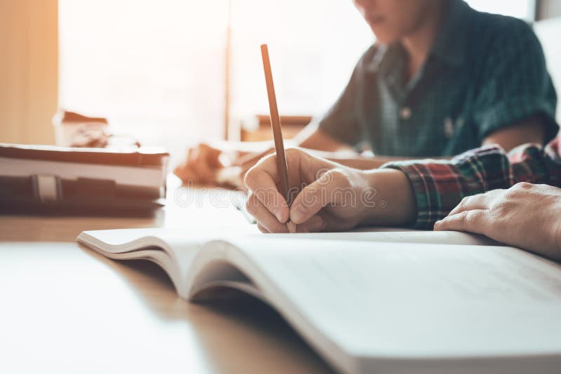 El estudiante está estudiando el papel y está escribiendo la prueba en sala de clase moderna imagen de archivo