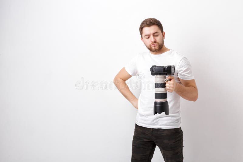 El fotógrafo profesional joven en camisa sostiene la cámara digital pesada con la lente larga Trabajo duro imágenes de archivo libres de regalías El fotógrafo profesional joven en camisa sostiene la cámara digital pesada con la lente larga Trabajo duro imágenes de archivo libres de regalías