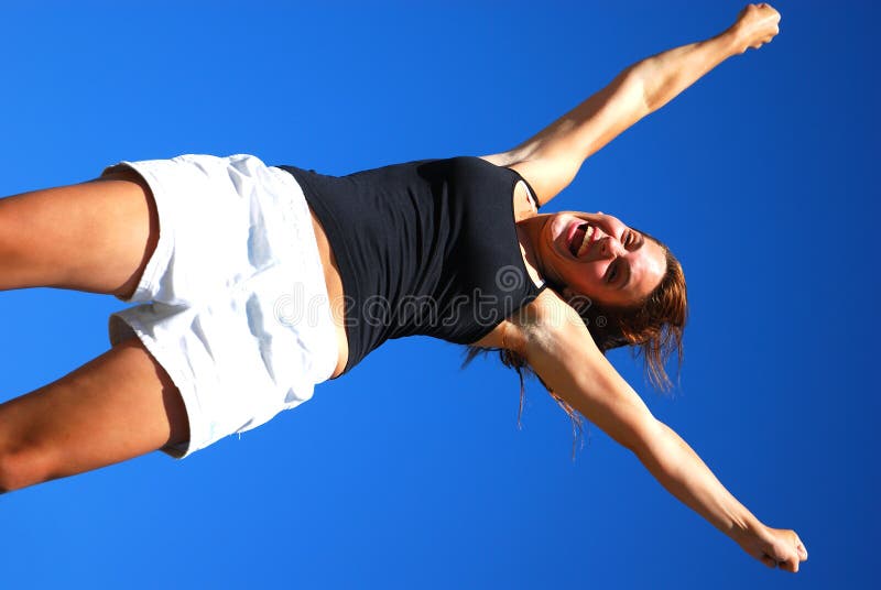 A beautiful caucasian white teenage athlete in her sports clothes with happy laughing facial expression jumping up and raising her arms in front of blue sky background after winning the race. A beautiful caucasian white teenage athlete in her sports clothes with happy laughing facial expression jumping up and raising her arms in front of blue sky background after winning the race