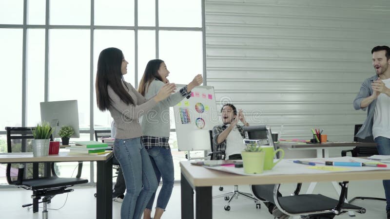 El grupo de mujeres de negocios creativas asiáticas felices alegres y los hombres gozan y teniendo baile de la diversión mientras metrajes