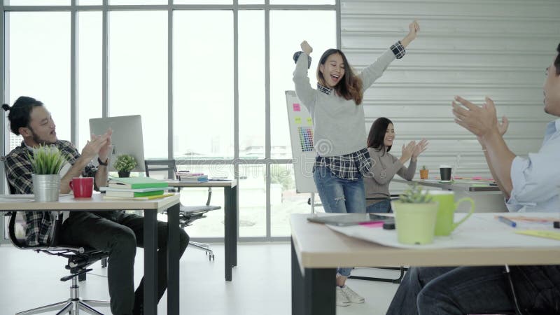 El grupo de mujeres de negocios creativas asiáticas felices alegres y los hombres gozan y teniendo baile de la diversión mientras almacen de metraje de vídeo