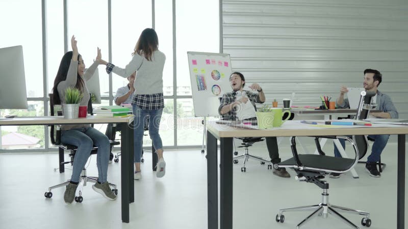 El grupo de mujeres de negocios creativas asiáticas felices alegres y los hombres gozan y teniendo baile de la diversión mientras almacen de metraje de vídeo