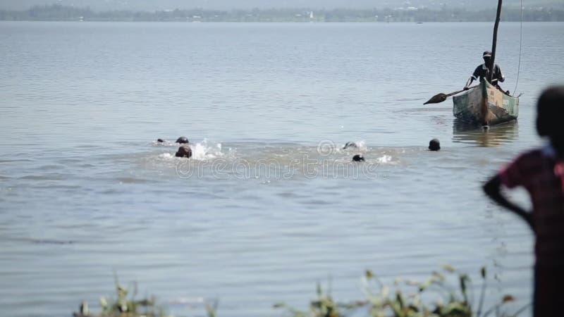 El grupo de niños africanos, muchachos está nadando en el lago, flotador detrás del barco