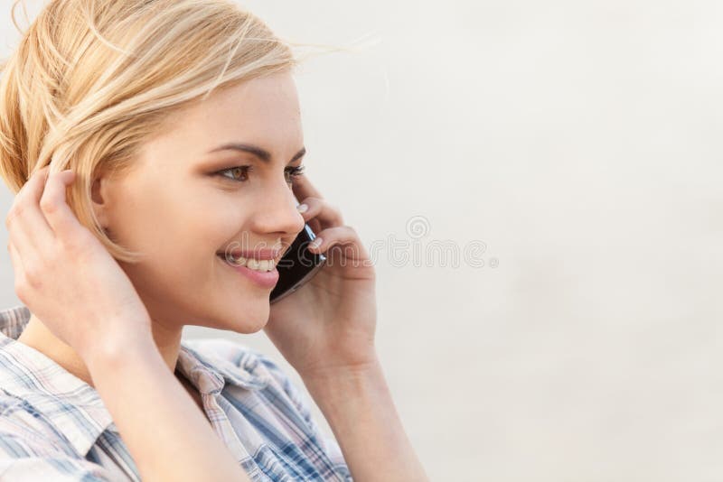 El hablar bastante rubio en el teléfono móvil y sonrisa imagen de archivo El hablar bastante rubio en el teléfono móvil y sonrisa imagen de archivo