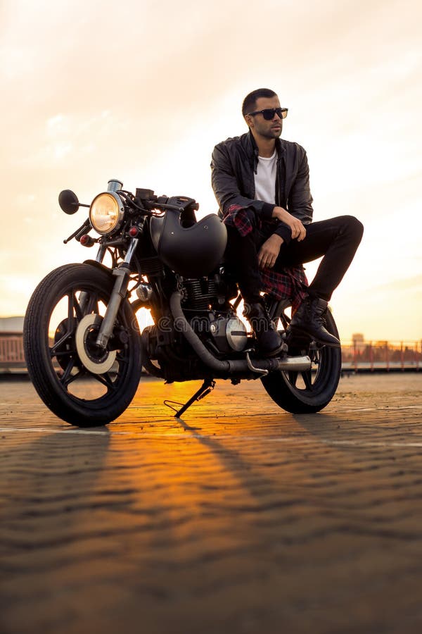 El hombre brutal se sienta en la moto de la aduana del corredor del café imagen de archivo libre de regalías El hombre brutal se sienta en la moto de la aduana del corredor del café imagen de archivo libre de regalías