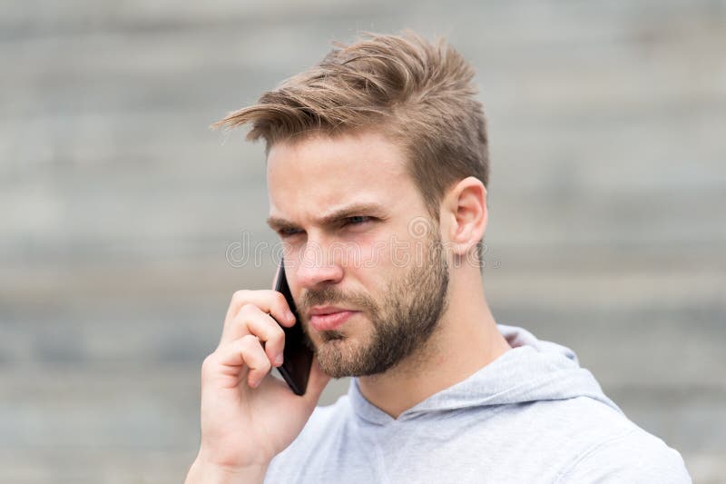El hombre con la barba camina con el smartphone, fondo urbano con las escaleras El hombre con la barba en cara seria habla en sma foto de archivo El hombre con la barba camina con el smartphone, fondo urbano con las escaleras El hombre con la barba en cara seria habla en sma foto de archivo