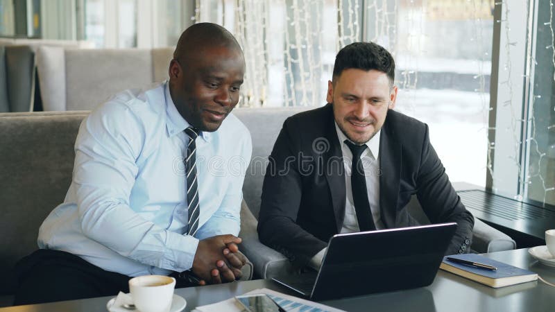 El hombre de negocios afroamericano alegre en ropa formal que discute negocio proyecta con su colega caucásico en el suyo