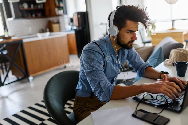 El hombre de negocios barbudo joven se está sentando delante del ordenador, trabajando El Freelancer, empresario trabaja en casa imágenes de archivo libres de regalías El hombre de negocios barbudo joven se está sentando delante del ordenador, trabajando El Freelancer, empresario trabaja en casa imágenes de archivo libres de regalías