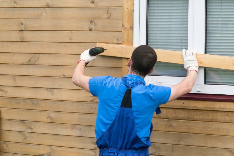 El hombre en batas cierra ventanas con los tableros para proteger la casa foto de archivo libre de regalías El hombre en batas cierra ventanas con los tableros para proteger la casa foto de archivo libre de regalías