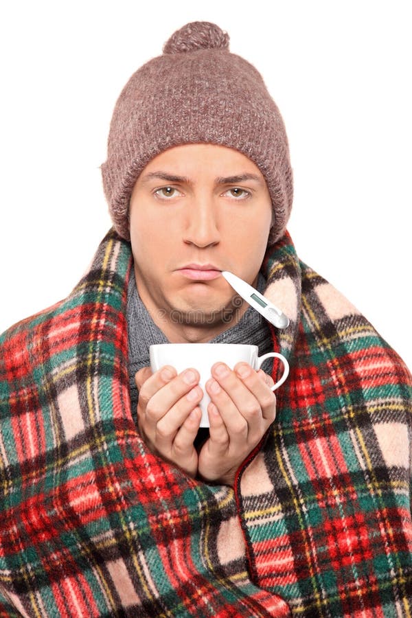 Ill man covered with blanket holding a tea cup and thermometer in his mouth isolated on white background. Ill man covered with blanket holding a tea cup and thermometer in his mouth isolated on white background
