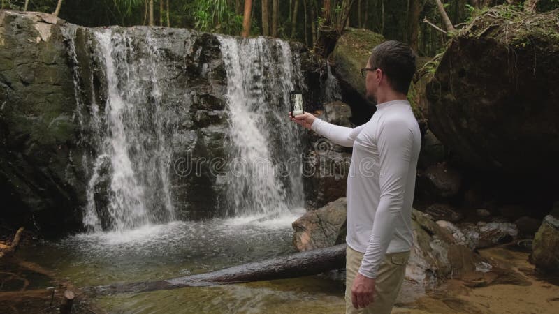 El hombre está filmando cascadas en el bosque por teléfono móvil