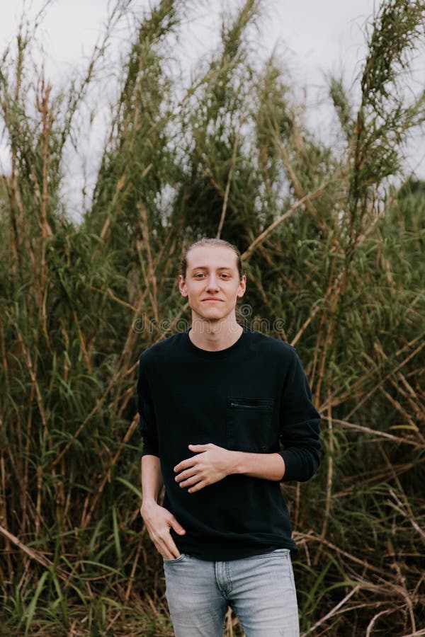 El hombre joven alto y hermoso con el pelo largo tiró detrás de modelado delante de exterior alto mismo de la hierba en natural imágenes de archivo libres de regalías El hombre joven alto y hermoso con el pelo largo tiró detrás de modelado delante de exterior alto mismo de la hierba en natural imágenes de archivo libres de regalías