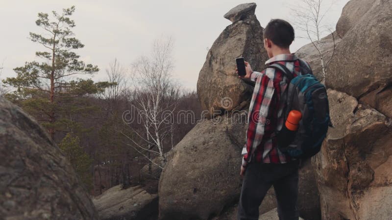 El hombre joven en una camisa a cuadros se coloca en el top de la roca grande y toma varios tiros del paisaje asombroso Ningunas