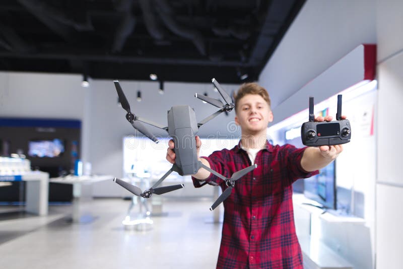 El hombre joven positivo lleva a cabo un quadcopter en sus manos y un panel de control en el fondo de la tienda foto de archivo libre de regalías El hombre joven positivo lleva a cabo un quadcopter en sus manos y un panel de control en el fondo de la tienda foto de archivo libre de regalías