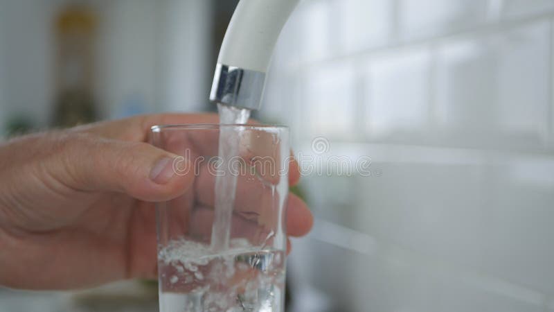 El hombre llena un vidrio del agua dulce del grifo de la cocina fotografía de archivo El hombre llena un vidrio del agua dulce del grifo de la cocina fotografía de archivo