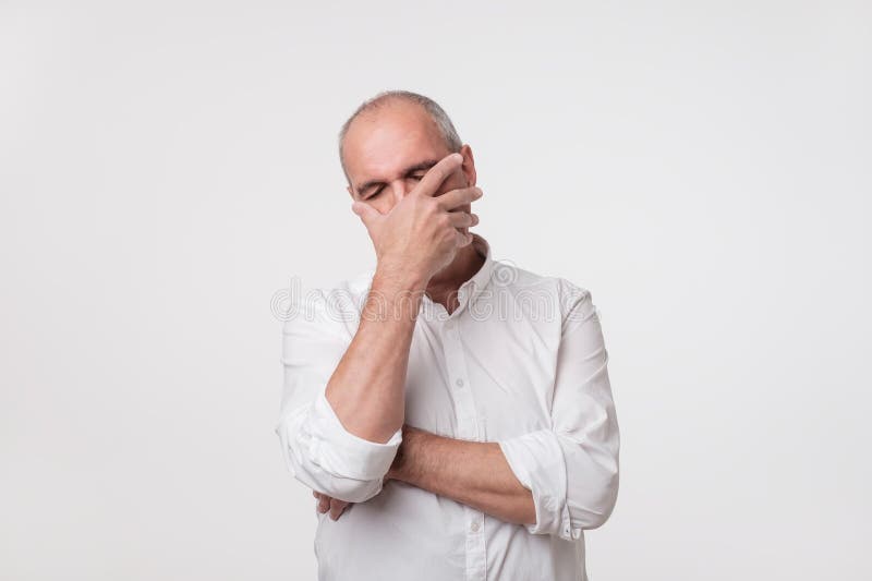 El hombre maduro descontentado en la camisa blanca que cubre su cara con entrega el fondo gris imagen de archivo libre de regalías El hombre maduro descontentado en la camisa blanca que cubre su cara con entrega el fondo gris imagen de archivo libre de regalías