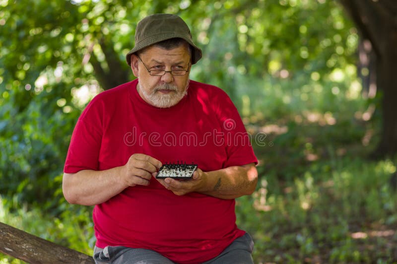 El hombre mayor que lleva la camiseta roja piensa sobre próximo paso mientras que juega a mini-ajedrez imágenes de archivo libres de regalías El hombre mayor que lleva la camiseta roja piensa sobre próximo paso mientras que juega a mini-ajedrez imágenes de archivo libres de regalías