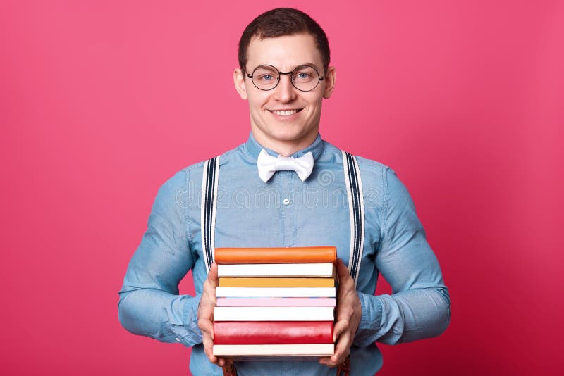 El hombre positivo sonriente sostiene el manojo de libros coloridos en ambas manos, presentación aisladas sobre fondo rosado en e imagen de archivo libre de regalías El hombre positivo sonriente sostiene el manojo de libros coloridos en ambas manos, presentación aisladas sobre fondo rosado en e imagen de archivo libre de regalías