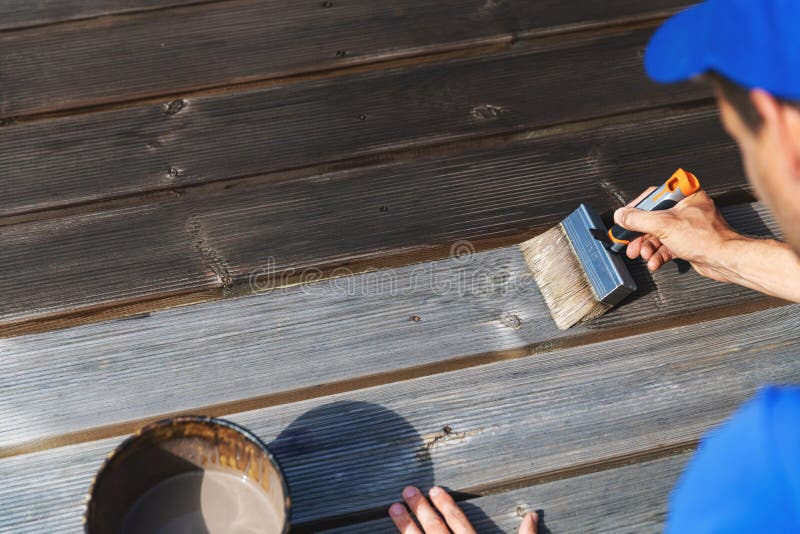 El hombre restaura la cubierta de madera del patio con la pintura protectora de madera fotos de archivo El hombre restaura la cubierta de madera del patio con la pintura protectora de madera fotos de archivo