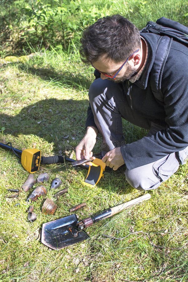 El hombre se sostiene en su mano que un objeto encontró en la tierra Un detector de metales y una pala mienten al lado de él fotografía de archivo libre de regalías El hombre se sostiene en su mano que un objeto encontró en la tierra Un detector de metales y una pala mienten al lado de él fotografía de archivo libre de regalías
