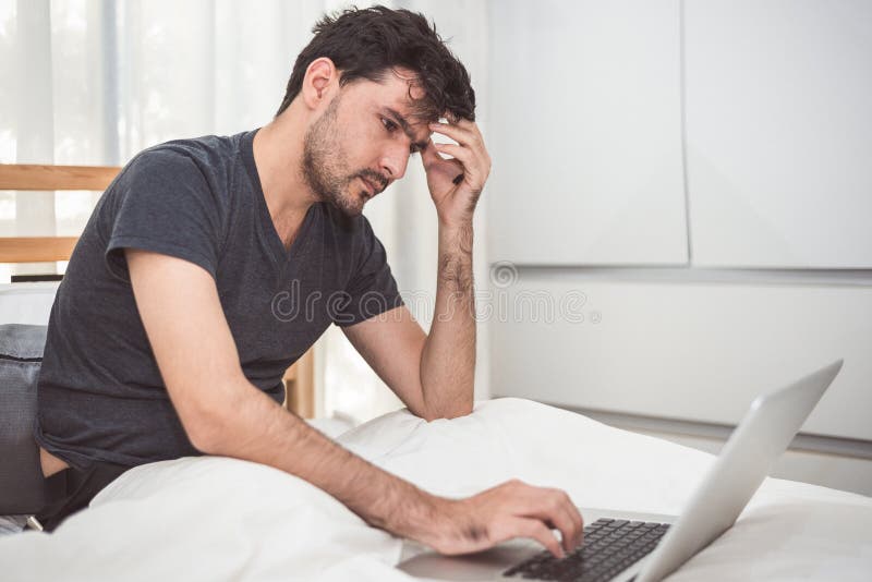 El hombre subrayó hacia fuera de trabajo con el ordenador portátil en dormitorio Tecnología foto de archivo El hombre subrayó hacia fuera de trabajo con el ordenador portátil en dormitorio Tecnología foto de archivo