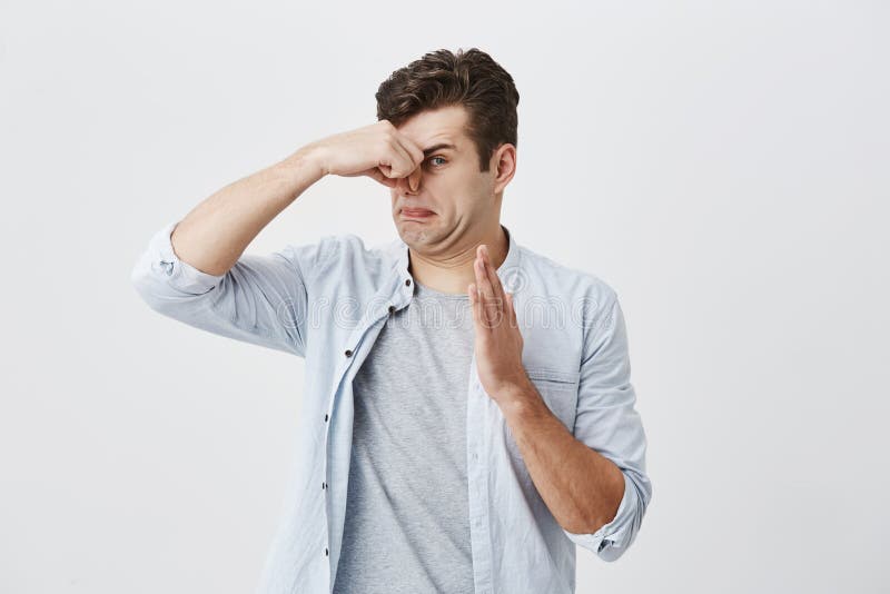 El inconformista masculino caucásico con el pelo oscuro se vistió en camisa azul clara sobre la camiseta gris que pellizcaba la n fotografía de archivo El inconformista masculino caucásico con el pelo oscuro se vistió en camisa azul clara sobre la camiseta gris que pellizcaba la n fotografía de archivo