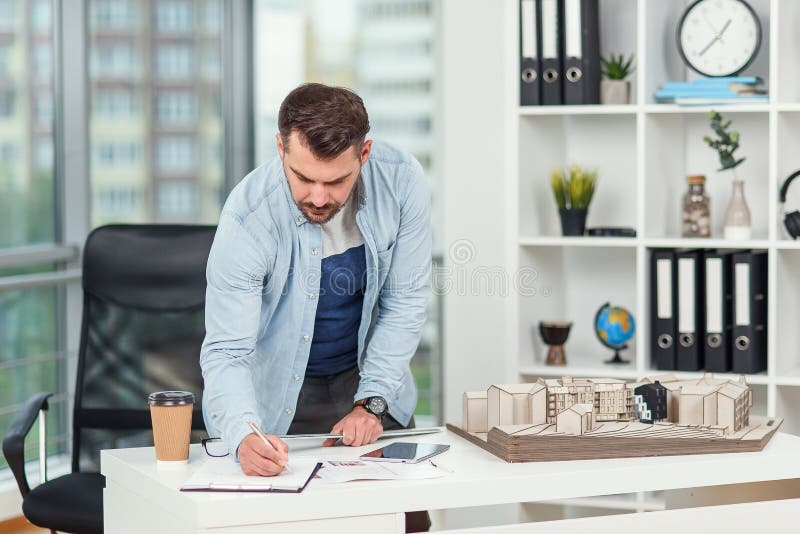 El ingeniero barbudo hermoso trabaja en proyectos de construcción examina el modelo en el que él trabaja y señala algunas dimensio foto de archivo libre de regalías
