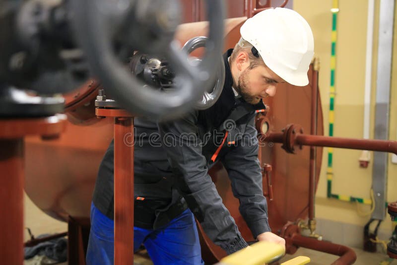 El ingeniero da vuelta a la válvula de puerta en sitio de caldera Operador del técnico en la estación de calefacción que trabaja foto de archivo El ingeniero da vuelta a la válvula de puerta en sitio de caldera Operador del técnico en la estación de calefacción que trabaja foto de archivo