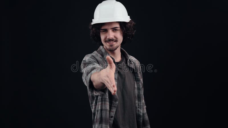 El ingeniero novato benévolo con casco blanco extiende su mano amistosa para saludar. aislado en fondo negro metrajes