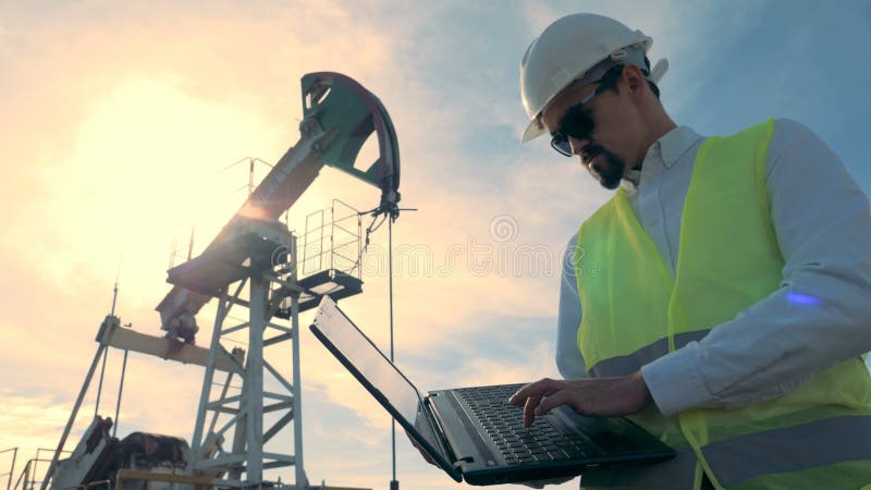 El inspector de la gasolina está trabajando con un ordenador cerca de una aceite-torre de perforación de bombeo, bomba de aceite