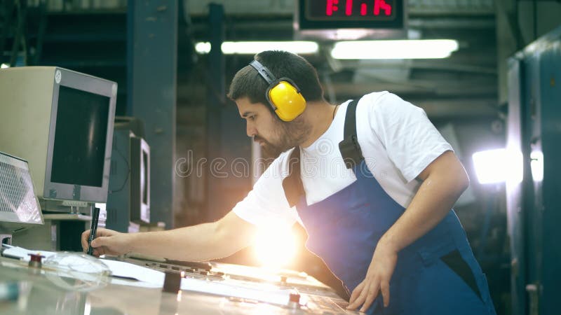 El inspector masculino está trabajando con diseños y un panel de control. ingeniero en instalaciones de fábrica.