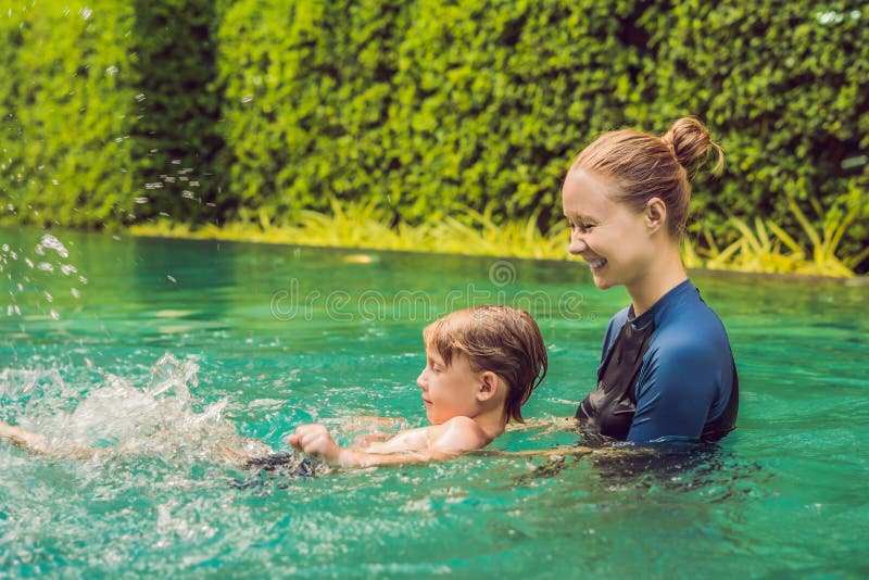 El instructor de la natación de la mujer para los niños está enseñando a un muchacho feliz a nadar en la piscina