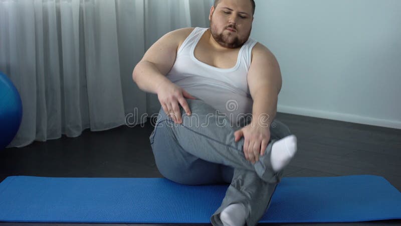 Hombre de vientre gordo poniéndose calcetines sentado en el suelo