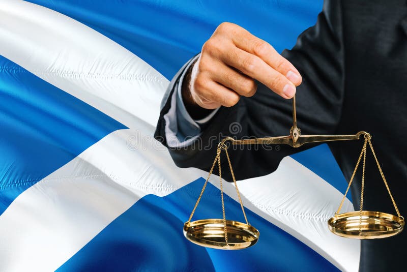 El juez escocés está sosteniendo escalas de oro de la justicia con el fondo de la bandera de Escocia que agita Tema de la igualda imagenes de archivo El juez escocés está sosteniendo escalas de oro de la justicia con el fondo de la bandera de Escocia que agita Tema de la igualda imagenes de archivo