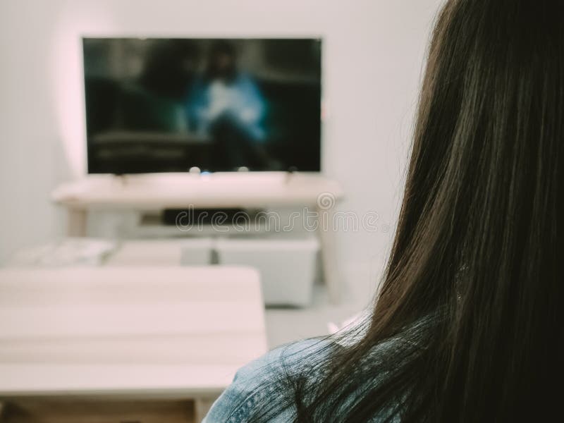 El lado trasero de la mujer del pelo negro sienta, relaja y ve la TV en su liv fotos de archivo libres de regalías El lado trasero de la mujer del pelo negro sienta, relaja y ve la TV en su liv fotos de archivo libres de regalías