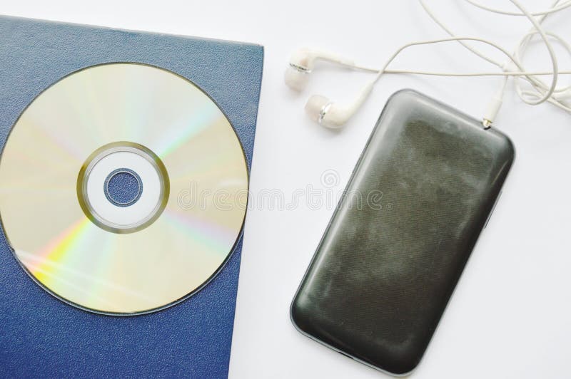 El libro y el CD-ROM con los auriculares conectan en smartphone en el fondo blanco foto de archivo El libro y el CD-ROM con los auriculares conectan en smartphone en el fondo blanco foto de archivo