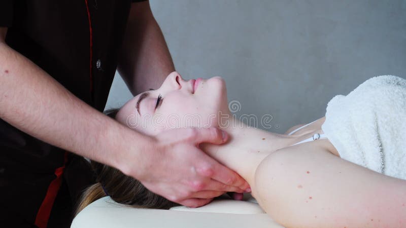 El masajista del individuo amasa el cuello de la chica joven, que miente en el sofá en sitio brillante de la cosmetología