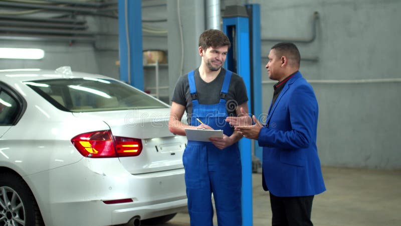 El mecánico muestra los daños en el coche al propietario y discute el precio de la reparación