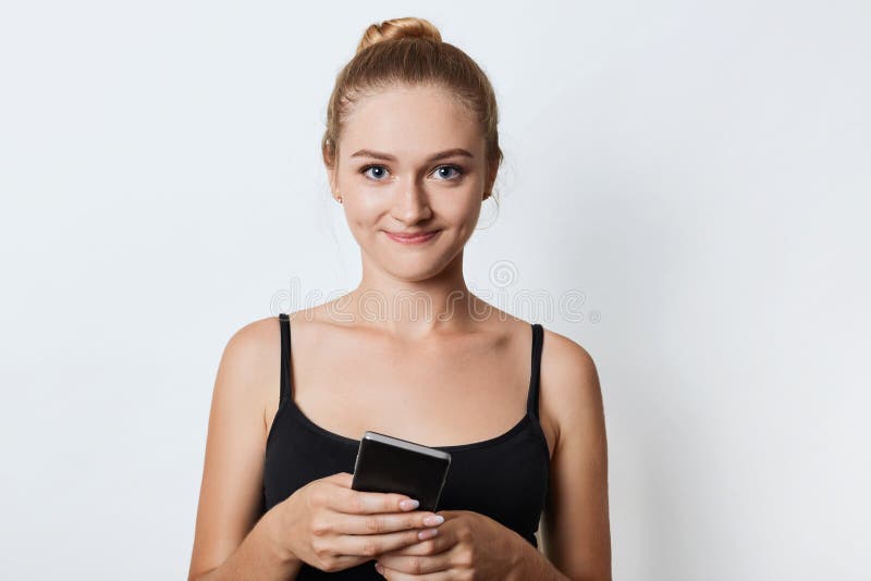 El modelo femenino joven lindo vestido ocasional, tiene pelo ligero atado en el nudo, teléfono elegante de los controles como esp foto de archivo El modelo femenino joven lindo vestido ocasional, tiene pelo ligero atado en el nudo, teléfono elegante de los controles como esp foto de archivo