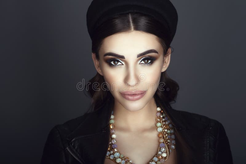 El modelo oscuro-cabelludo atractivo con hermoso compone y pelo liso que lleva el sombrero negro del fortín, la chaqueta de cuero foto de archivo libre de regalías El modelo oscuro-cabelludo atractivo con hermoso compone y pelo liso que lleva el sombrero negro del fortín, la chaqueta de cuero foto de archivo libre de regalías