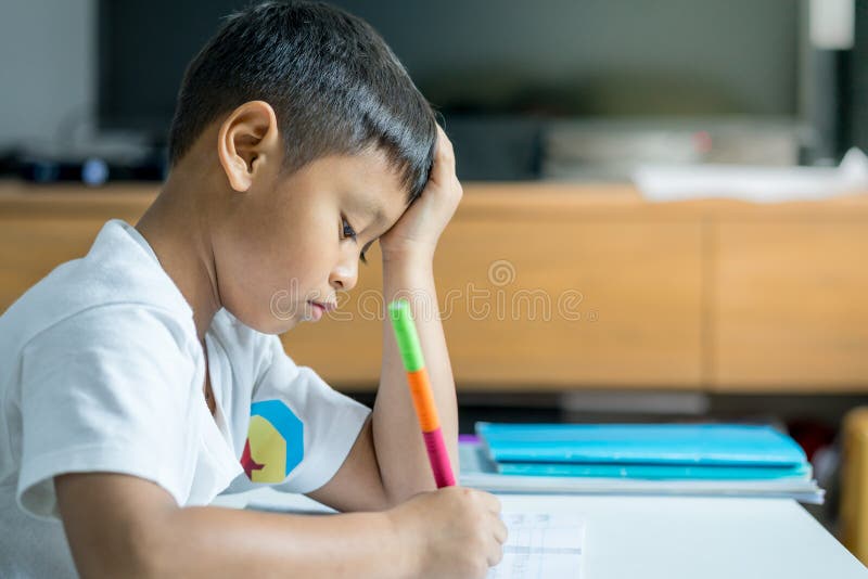El muchacho asiático joven escribe en el cuaderno por el lápiz en el cuarto foto de archivo libre de regalías El muchacho asiático joven escribe en el cuaderno por el lápiz en el cuarto foto de archivo libre de regalías