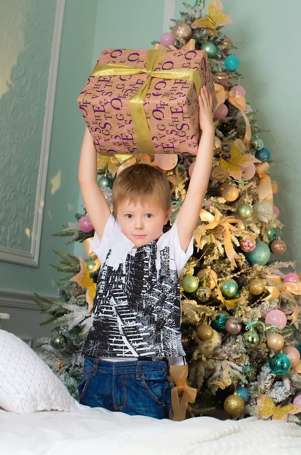 El muchacho con la caja de regalo en manos acerca al árbol imagenes de archivo El muchacho con la caja de regalo en manos acerca al árbol imagenes de archivo