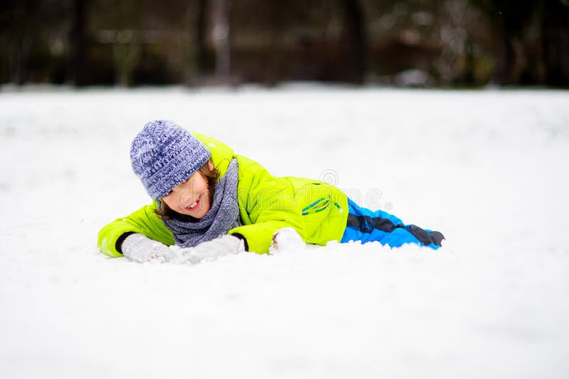 El muchacho de la edad de escuela en guardapolvos brillantes del invierno miente en nieve fotografía de archivo El muchacho de la edad de escuela en guardapolvos brillantes del invierno miente en nieve fotografía de archivo