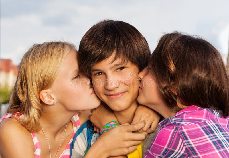 Two girls kissing smiling cute boy in cheeks in close up view. Two girls kissing smiling cute boy in cheeks in close up view